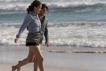 Feliz pareja joven y romántica caminando en la playa - foto de stock