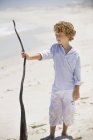 Хлопчик тримає дерев'яною палицею на піщаному пляжі — стокове фото