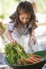 Милая маленькая девочка кладет морковь в тачку — стоковое фото