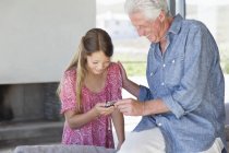 Смеющийся мужчина показывает сообщение с мобильного телефона внучке — стоковое фото