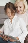 Женщина помогает дочери в использовании цифрового планшета — стоковое фото