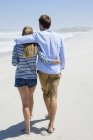 Visão traseira do casal romântico andando na praia sob o céu azul — Fotografia de Stock