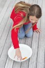 Girl touching red fish in bowl on wooden pier — Stock Photo