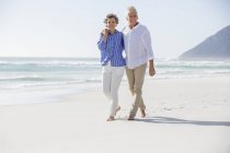 Embracing happy couple walking on sandy beach — Stock Photo