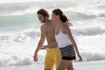 Счастливая молодая пара, гуляющая по пляжу с волнистым морем на фоне — стоковое фото