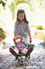 Linda niña empujando carretilla con juguetes al aire libre - foto de stock