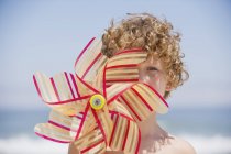 Portrait of boy holding pinwheel in front of face on beach — Stock Photo