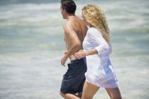 Mid adult couple running on beach together — Stock Photo