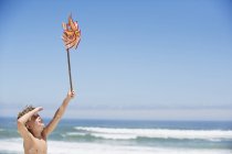 Garçon tenant pinwheel sur la plage sous le ciel bleu — Photo de stock