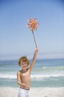 Retrato de niño sosteniendo un molinete en la playa bajo el cielo azul - foto de stock
