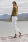 Mujer joven de pie en la cubierta en la orilla del lago - foto de stock