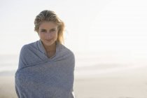 Portrait of relaxed blond woman standing on beach wrapped with shawl — Stock Photo