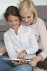 Жінка допомагає доньці використовувати цифровий планшет — стокове фото