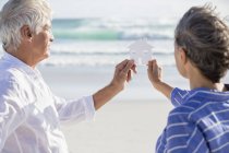 Close-up of senior couple holding paper home on beach — Stock Photo