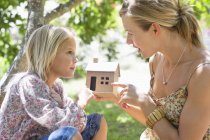 Little girl and mother holding dollhouse outdoors — Stock Photo