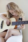Menina bonito sentado na poltrona e tocando uma guitarra — Fotografia de Stock