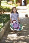 Cute little girl pushing wheelbarrow with toys outdoors — Stock Photo