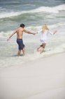 Allegra coppia che corre sulla spiaggia nel mare ondulato — Foto stock