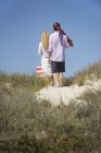 Visão traseira do casal andando na praia com saco listrado e guarda-chuva de praia — Fotografia de Stock