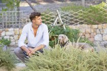 Созерцательный мужчина с собакой, отдыхающей в саду — стоковое фото