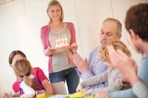 Familie bei einer Geburtstagsfeier mit einer Frau, die im Hintergrund Kuchen bringt — Stockfoto