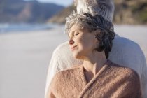 Nahaufnahme eines entspannten, nachdenklichen Senioren-Paares, das Rücken an Rücken am Strand steht — Stockfoto