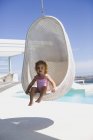Baby girl sitting in wicker swing near swimming pool — Stock Photo