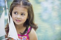 Задумлива маленька дівчинка сидить тримаючи іграшковий човен і дивлячись геть — стокове фото
