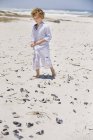 Garçon collecte coquillages sur la plage de sable fin — Photo de stock