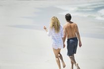Vista trasera de la pareja caminando por la playa cogidos de la mano - foto de stock