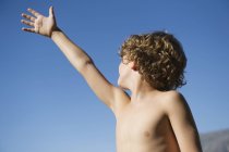 Netter kleiner Junge hebt die Hand gegen den klaren Himmel — Stockfoto