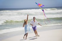 Пара веселится с летающим воздушным змеем на пляже — стоковое фото