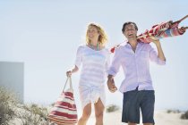 Couple heureux marchant sur la plage tenant la main avec sac et parasol — Photo de stock