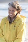 Ritratto di donna matura felice in impermeabile in piedi sulla spiaggia — Foto stock