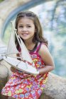 Усміхнена маленька дівчинка сидить у басейні з іграшковим човном — стокове фото