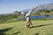 Bonito menino fazendo cartwheel na grama na natureza contra montanhas — Fotografia de Stock
