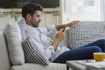 Homem pensativo sentado no sofá e usando smartphone — Fotografia de Stock