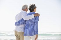 Vista posteriore di abbracciare coppia anziana a piedi sulla spiaggia — Foto stock