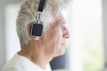 Старший чоловік слухає музику з навушниками і дивиться вбік — стокове фото
