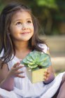 Petite fille mignonne tenant la plante en pot et levant les yeux — Photo de stock