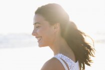 Jeune femme souriante avec les yeux fermés sur la plage au soleil — Photo de stock