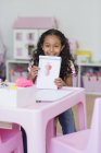 Glückliches kleines Mädchen zeigt Zeichnung am rosa Tisch — Stockfoto