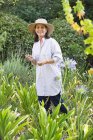 Donna sorridente in cappello di paglia che tiene fiori in un giardino — Foto stock