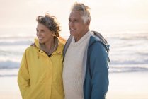 Feliz pareja de ancianos de pie en la playa al atardecer - foto de stock
