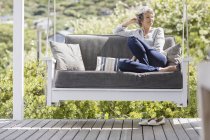 Glücklich ältere Frau sitzt auf Schaukel in Veranda — Stockfoto