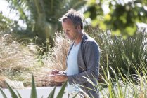 Reifer Mann benutzt Handy im sonnigen Garten — Stockfoto