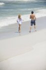 Vista trasera de la pareja corriendo en la playa de arena - foto de stock