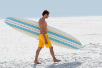 Perfil lateral de un hombre que lleva tabla de surf en la playa - foto de stock