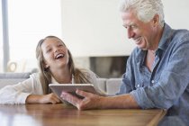 Mädchen lacht, während Opa digitales Tablet am Schreibtisch benutzt — Stockfoto