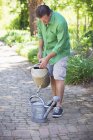 Человек наливает воду в банку для полива в саду — стоковое фото